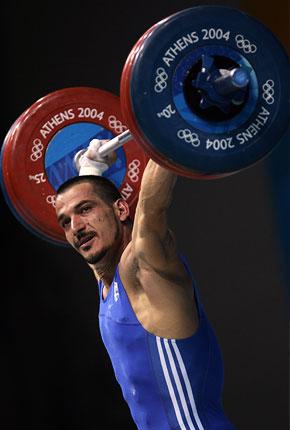 Athens, 21 August 2004, Games of the XXVIII Olympiad. Pyrros DIMAS of Greece looks across into the crowd as he completes a lift in the men's -85kg category weightlifting competition at Nikaia Olympic Weightlifting Hall. Credit: Getty Images/Doug Pensinger