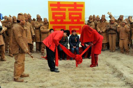 A Newly wedded couple take part in a special performance art wedding ceremony held in Zhengzhou, central China's Henan Province, Jan. 10, 2010. Students from Zhongyuan University of Technology presented an performance artwork on a wedding ceremony for a couple who come from farmer families on the bank of Huanghe River on Monday during which they perform in khaki-colored clothes representing the color of earth to show the struggle process of farmers' setting down in cities with their invariable distinctive character.(Xinhua/Liu Shuting)