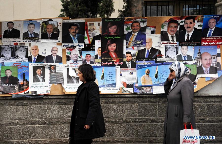 DAMASCUS, April 12, 2016 (Xinhua) -- Two Syrian women walk by the posters of candidates for Syria