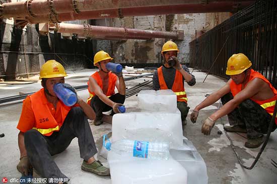 Workers drink icy water while resting near a pile of ice cubes at a construction site in Changzhou, East China