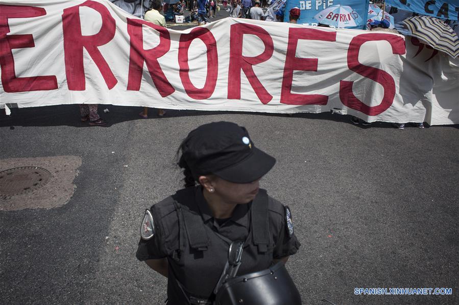 Una mujer policía monta guardia frente a una pancarta durante una jornada de ollas populares y acampe de militantes de la organización Movimiento Barrios de Pie junto a otras organizaciones, frente al Obelisco en Buenos Aires, Argentina, el 21 de febrero de 2017. La jornada de ollas populares y acampe se llevó a cabo en las avenidas Congreso y Retiro, Puente Pueyrredón y el Obelisco en Buenos Aires, y en distintos lugares del país en reclamo por la "discontinuidad" de planes sociales en el área del Ministerio de Trabajo, que según denunciaron los organizadores afectarán a unos 20,000 trabajadores, de acuerdo con información de la prensa local. (Xinhua/Martín Zabala)