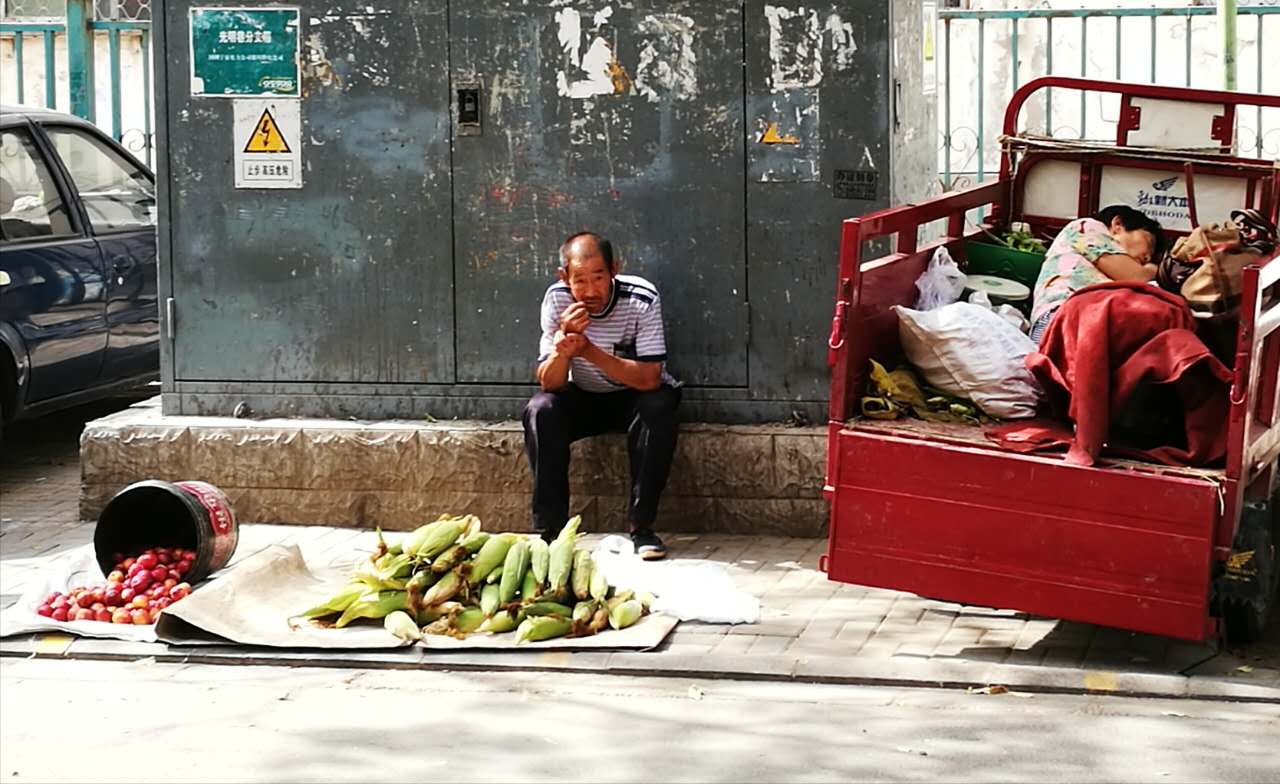 Man who is selling home-grown corn and tomatoes on street. (Photo/ Wang Yabo)