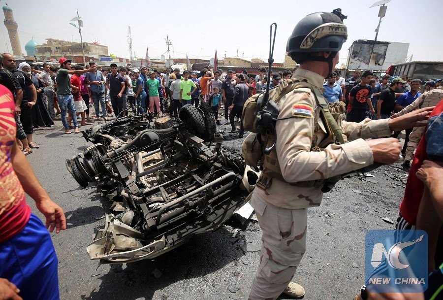 A member of the Iraqi security forces stands guard as civilians look at the damage following a car bomb attack in Sadr City, a Shiite area north of the capital Baghdad, on May 11, 2016. (Xinhua/AFP Photo)