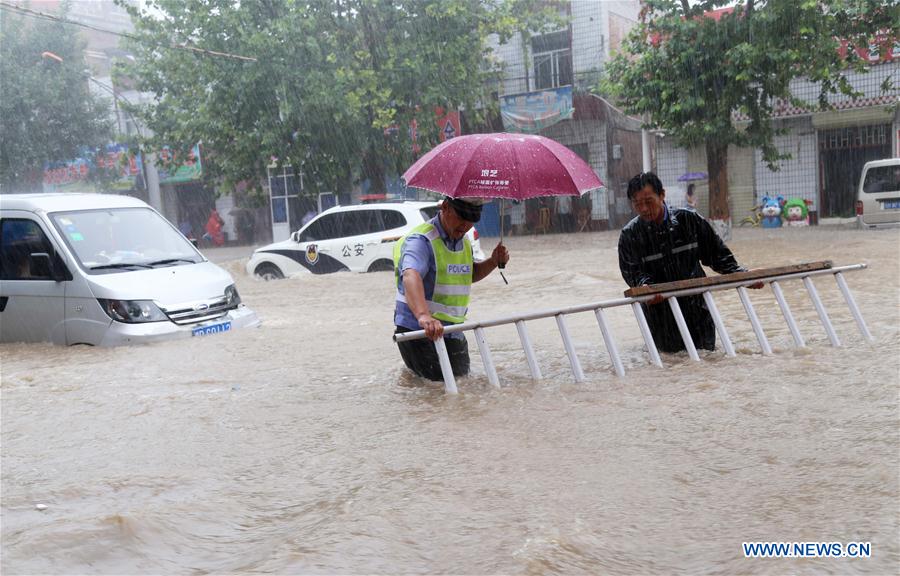 YUNCHENG, July 19, 2016 (Xinhua) -- Traffic policemen move away a barrier on a flooded road in Wanrong County, north China