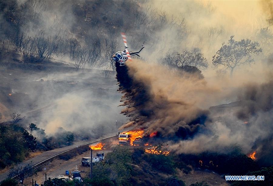 A helicopter tries to put out fire on a burning vehicle in San Bernardino County, California, the United States, Aug. 17, 2016. A fast-moving wildfire erupted Tuesday morning in San Bernardino County, southern California, ripping through over 30,000 acres of hills within one day and forcing more than 82,000 people to evacuate. [Photo: Xinhua/Zhang Chaoqun]