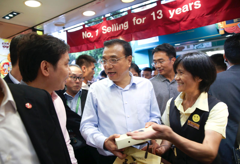 Chinese Premier Li Keqiang talks with owners of a dessert shop at Rua da Cunha, an ancient business street in Macao on October 11, 2016. He visited several shops on the pedestrian street, bought a box of egg tarts, a box of walnut cakes and a postcard. Li also posed for photos with local residents and tourists. [Photo: gov.cn]