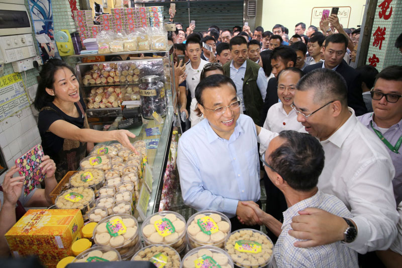Chinese Premier Li Keqiang talks with an owner of a dessert shop at Rua da Cunha, an ancient business street in Macao. He visited several shops on the pedestrian street, bought a box of egg tarts, a box of walnut cakes and a postcard. Li also posed for photos with local residents and tourists. [Photo: gov.cn] 
