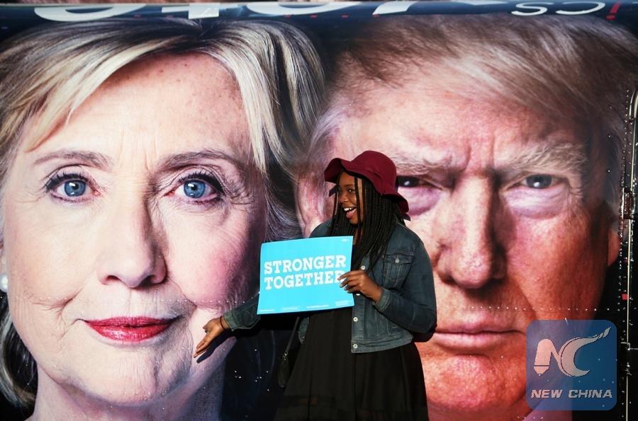 A girl poses for photos with Hillary Clinton and Donald Trump posters at Hofstra University in New York, the United States on Sept. 26, 2016. (Xinhua Photo)