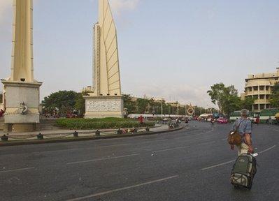 A western tourist makes his way past Bangkok's Democracy Monument and past an anti-government demonstration staging area Tuesday, March 16, 2010, in Bangkok, Thailand. Business leaders say the constant political turmoil continues to hurt the tourism industry as well as other areas. (AP Photo/David Longstreath) 