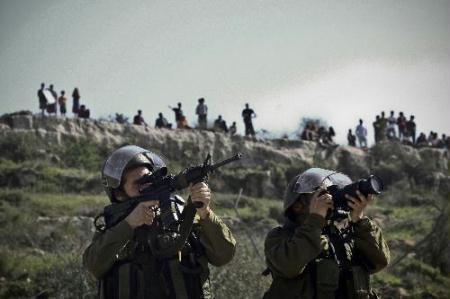 An Israeli soldier points gun to Palestinians during a protest against the confiscation of lands at the West Bank village of Nabi Salah in northern Ramallah, Feb. 12, 2010. (Xinhua/Fadi Arouri)