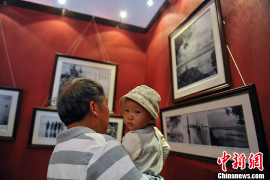 圖為爺爺抱著兒孫來看展覽，講述自己年輕時的故事。中新社發 任東攝