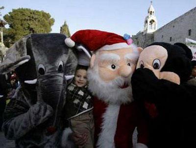 A Palestinian boy poses for a picture with people wearing elephant, mouse and Santa Claus costumes during a children Christmas parade near the Church of the Nativity, the site revered as the birthplace of Jesus, in the West Bank town of Bethlehem December 23, 2009.REUTERS/Ammar Awad