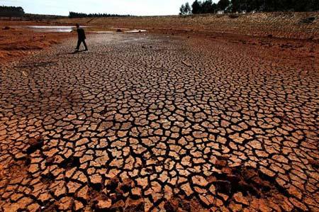 A farmer walks on the cracking bottom of a pond in Shilin County, southwest China's Kunming City, Feb. 2, 2010. (Xinhuanet File Photo)