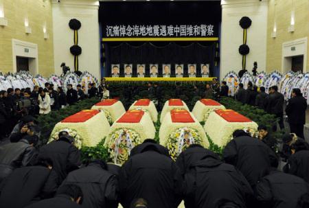 A final tribute at the Ministry of Public Security. A banner saying "Eternal Glory to the Heroes" hung with the portraits of the eight fallen peacekeepers. People wear white flowers as a sign of mourning. They stand in silent tribute and bow three times.