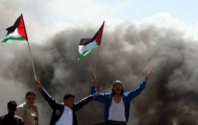 Palestinian youths wave their national flag and set tyres on fire as they clash with Israeli soldiers near the Gaza border. (AFP/Mahmud Hams)