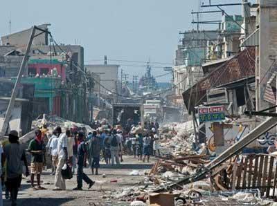 A navy ship is seen at the end of the street as Haitians walk around the rubble of Port au Prince, Haiti.(AFP/Paul J. Richards)