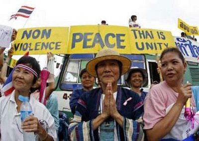 A woman offers a traditional Thai greeting as pro-government supporters hold placards and wave the Thai national flag during a counter-protest rally at the Victory monument in Bangkok April 17, 2010. REUTERS/Eric Gaillard