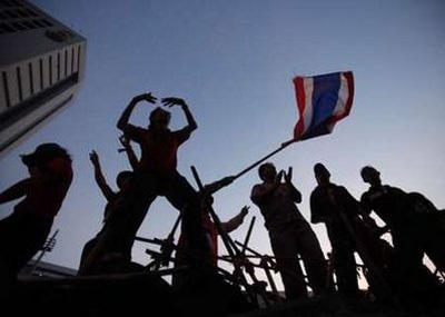 Anti-government "red shirt" protesters dance and wave a Thai national flag as they gather behind a barricade built with bamboo poles and tyres at an intersection close to the Silom Road financial district in Bangkok April 21, 2010. REUTERS/Chaiwat Subprasom