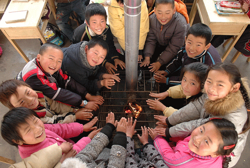 2009年1月6日，山東省日照市東港區南湖鎮盛家代疃希望小學三年級一班教室，小學生在火爐旁取暖。