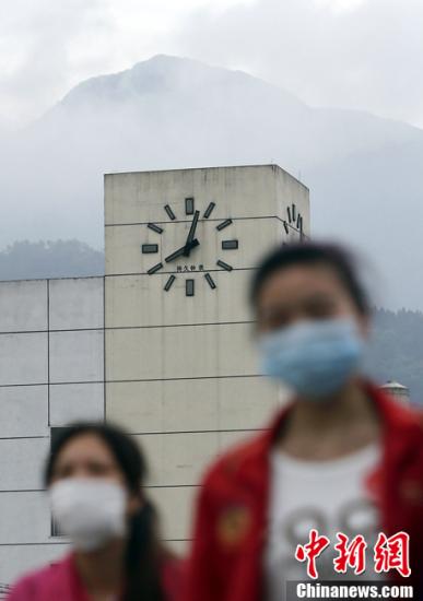 4月25日，兩名戴著口罩的女子從四川蘆山車站的時鐘前走過，時鐘一直停在發生地震的8點02分，目前震區防疫工作全面啟動，成為這一階段震區工作重點。中新社發 張浩 攝