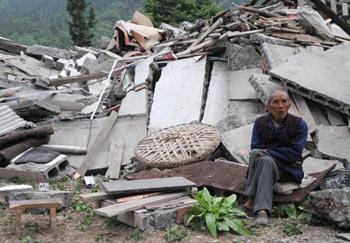 A local sits besides a collapsed house in the earthquake-affected Beichuan County, southwest China's Sichuan Province, on May 13, 2008. (Xinhua Photo)