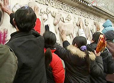 People patiently join a zigzagging queue to touch a lucky zodiac animal on the wall.