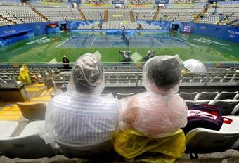 Spectators wait under the rain for the tennis tournament of the 2008 Beijing Olympic Games to begin, at the centre court of the Olympic Green Tennis Centre in Beijing on August 10, 2008.